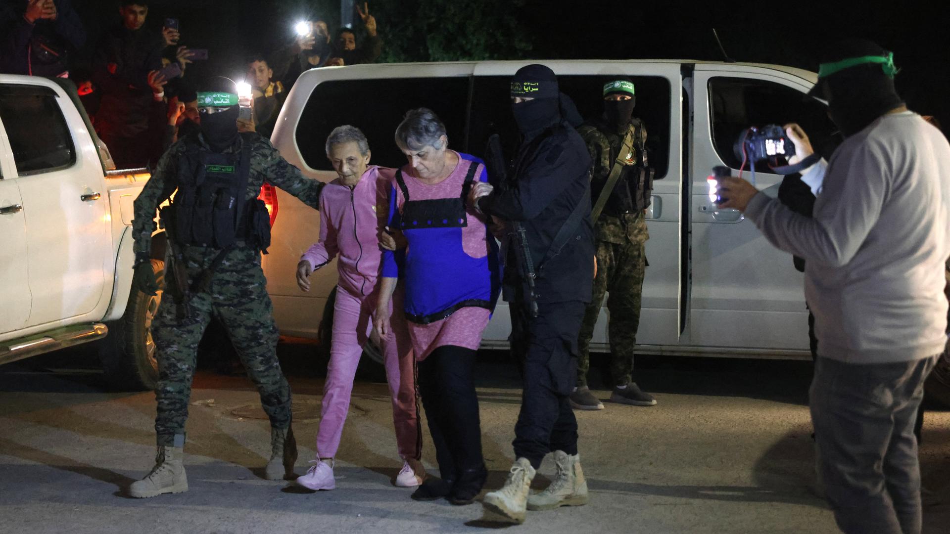 Maskierte und bewaffnete Männer führen zwei ältere Frauen ab.