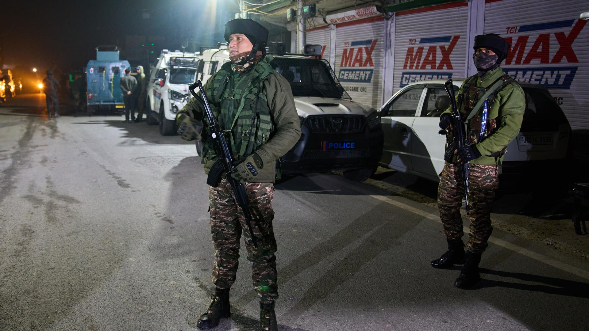 Zwei schwer bewaffnete Soldaten stehen auf einer Straße, an deren Rand Autos geparkt sind. Es ist Nacht, die beiden werden von einem Strahler beleuchtet. Zwei schwer bewaffnete Soldaten stehen auf einer Straße, an deren Rand Autos geparkt sind. Es ist Nacht, die beiden werden von einem Strahler beleuchtet.