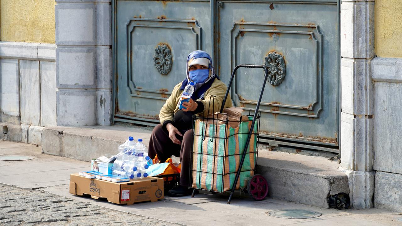 Eine Strassenverkäuferin in Alsancak, Izmir. Sie hat auf einer Pappkiste Plastikwasserflaschen und Taschentuchpackungen vor sich liegen.Türkei, 13. Februar 2022. 