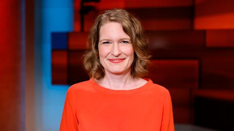 Porträt von Stefanie Lohaus im Fernsehstudio. Sie trägt einen orangen Pullover und hat rotblonde schulterlange Haare.