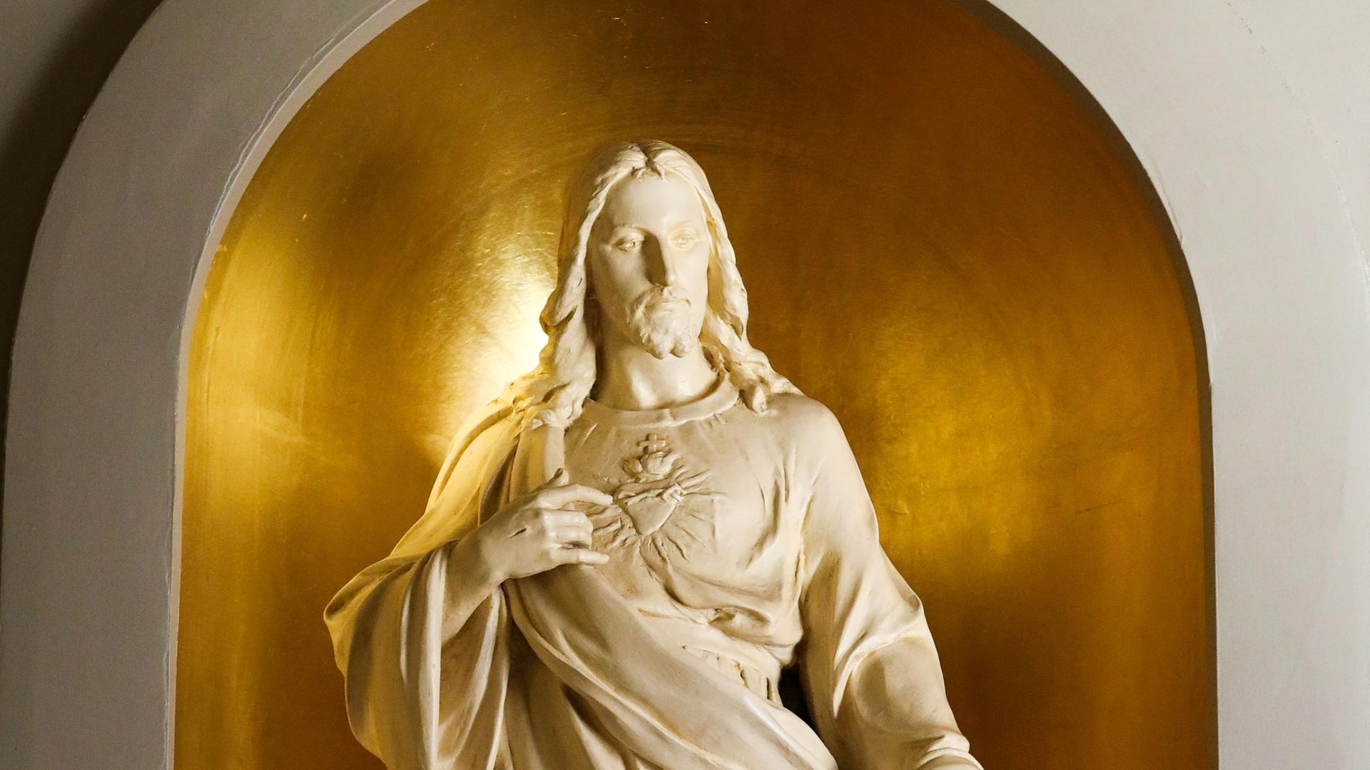 Eine weiße Jesusfigur steht in einer goldenen Nische. Sie verweist auf das deutlich ausgearbeitete Herz auf seiner Brust.