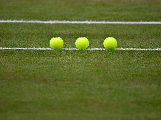 Nachaufnahme von drei Tennisbällen, die auf einem Tennisplatz sorgfältig aufgereiht liegen. 