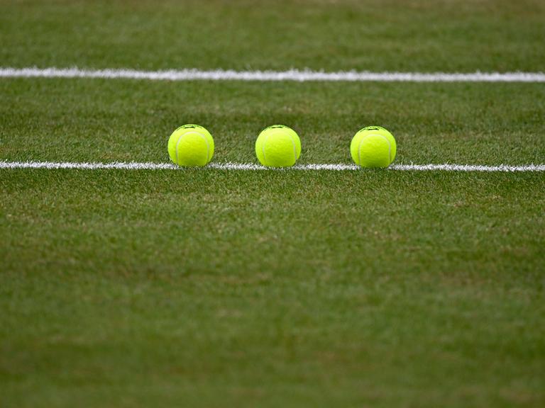 Nachaufnahme von drei Tennisbällen, die auf einem Tennisplatz sorgfältig aufgereiht liegen. 