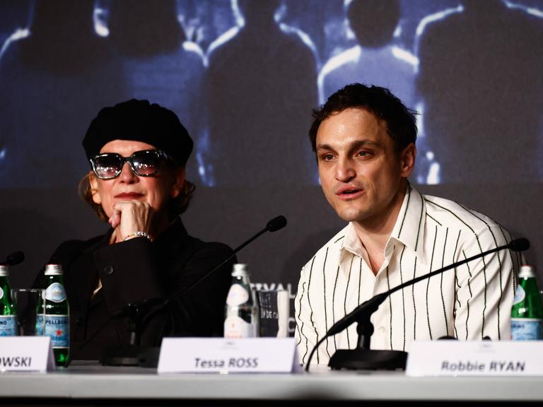 Der deutsche Schauspieler Franz Rogowski sitzt bei der Pressekonferenz zu dem britischen Film "Bird" in Cannes hinter einem Tisch neben der britischen Regisseurin Andrea Arnold und spricht in ein Mikrofon.