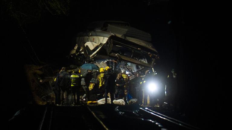 Helfer stehen um einen entgleisten, schwer beschädigten Zug in Spanien.