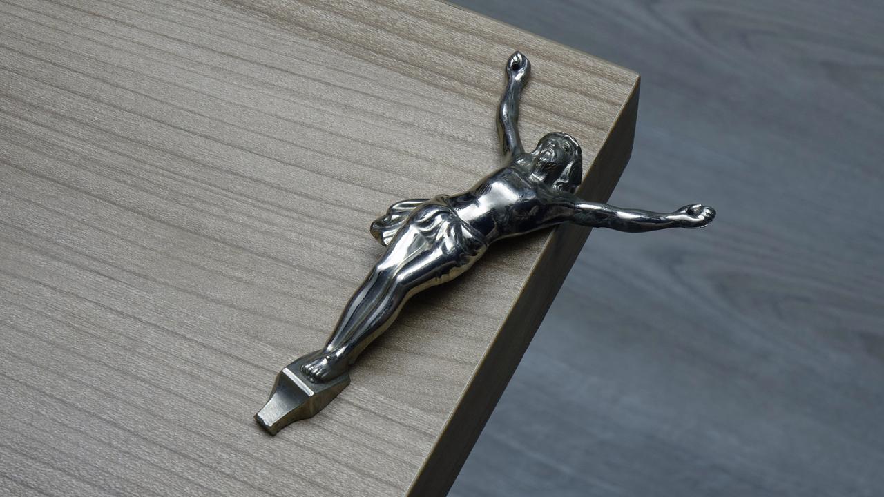 Eine von einem Kreuz gelöste Christusfigur liegt auf einer Tischkante