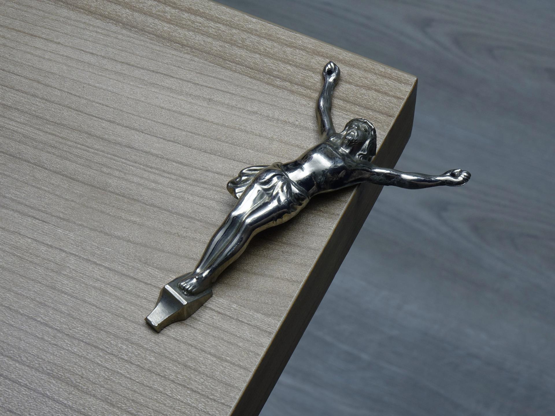 Eine von einem Kreuz gelöste Christusfigur liegt auf einer Tischkante