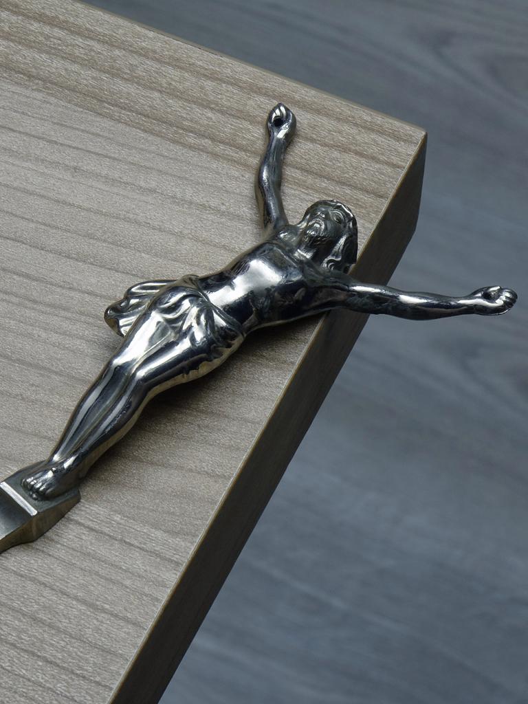Eine von einem Kreuz gelöste Christusfigur liegt auf einer Tischkante