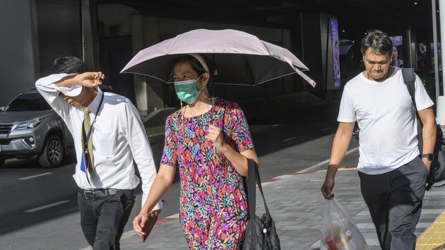 In Bangkok laufen Menschen über die Straße und versuchen sich mit einem Schirm oder dem Arm vor der Sonne zu schützen.