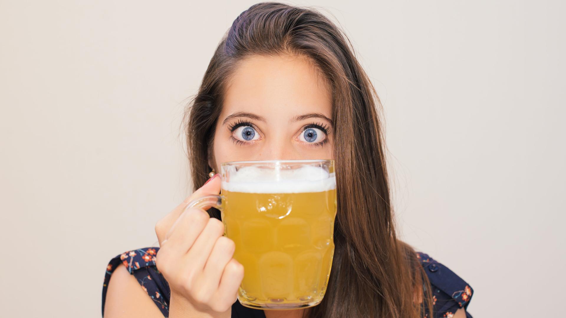 Eine junge Frau, deren untere Gesichtshälfte durch ein volles Bierglas verdeckt wird