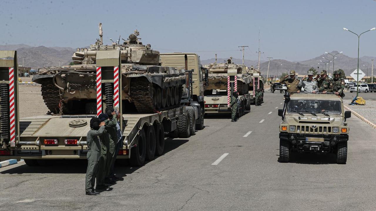 Das Bild zeigt militärische Fahrzeuge der iranischen Armee, die auf der Ladefläche von Lastwagen geladen sind