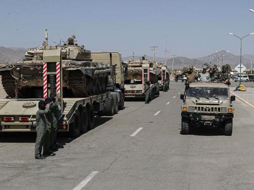 Das Bild zeigt militärische Fahrzeuge der iranischen Armee, die auf der Ladefläche von Lastwagen geladen sind