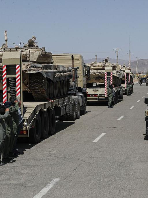 Das Bild zeigt militärische Fahrzeuge der iranischen Armee, die auf der Ladefläche von Lastwagen geladen sind