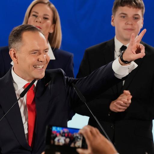 Mann in Anzug umringt von Menschen lacht und zeigt ein Victory-Zeichen: Polens kommender Präsident Karol Nawrocki feiert mit Anhängern seinen Wahlsieg.