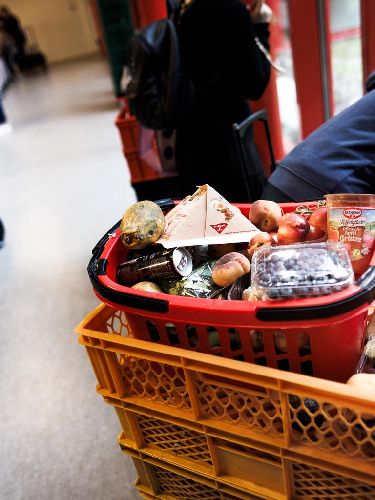Eine Frau sammelt Obst aus einer Kiste während andere an der Lebensmittelausgabe stehen in der Ausgabestelle Paul-Schneider-Haus der Berliner Tafel. 