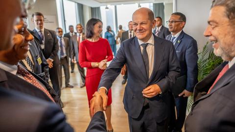 Bundeskanzler Olaf Scholz schüttelt auf einem Empfang Hände. Im Hintergrund ist Außenministerin Baerbock zu sehen.