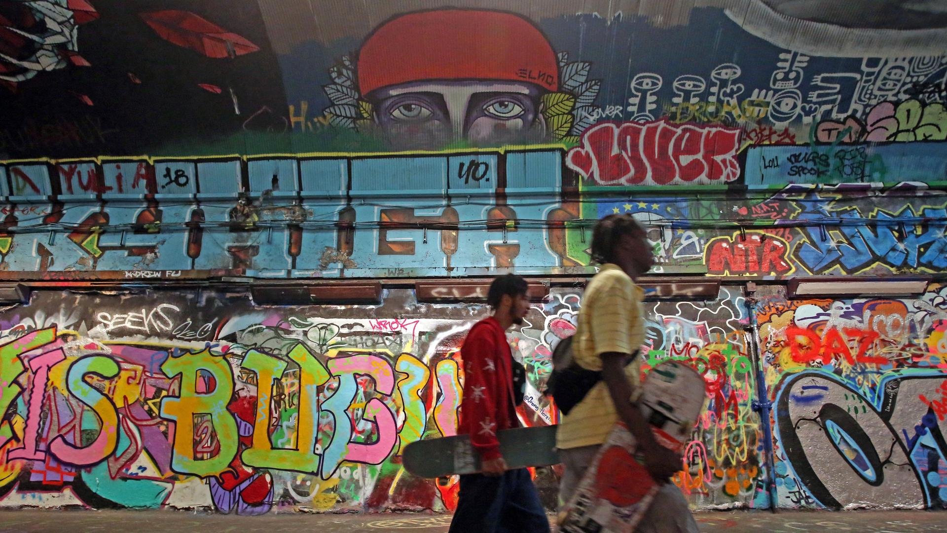 Skateboarders gehen an einer mit Graffiti bemalten Hauswand in London vorbei.