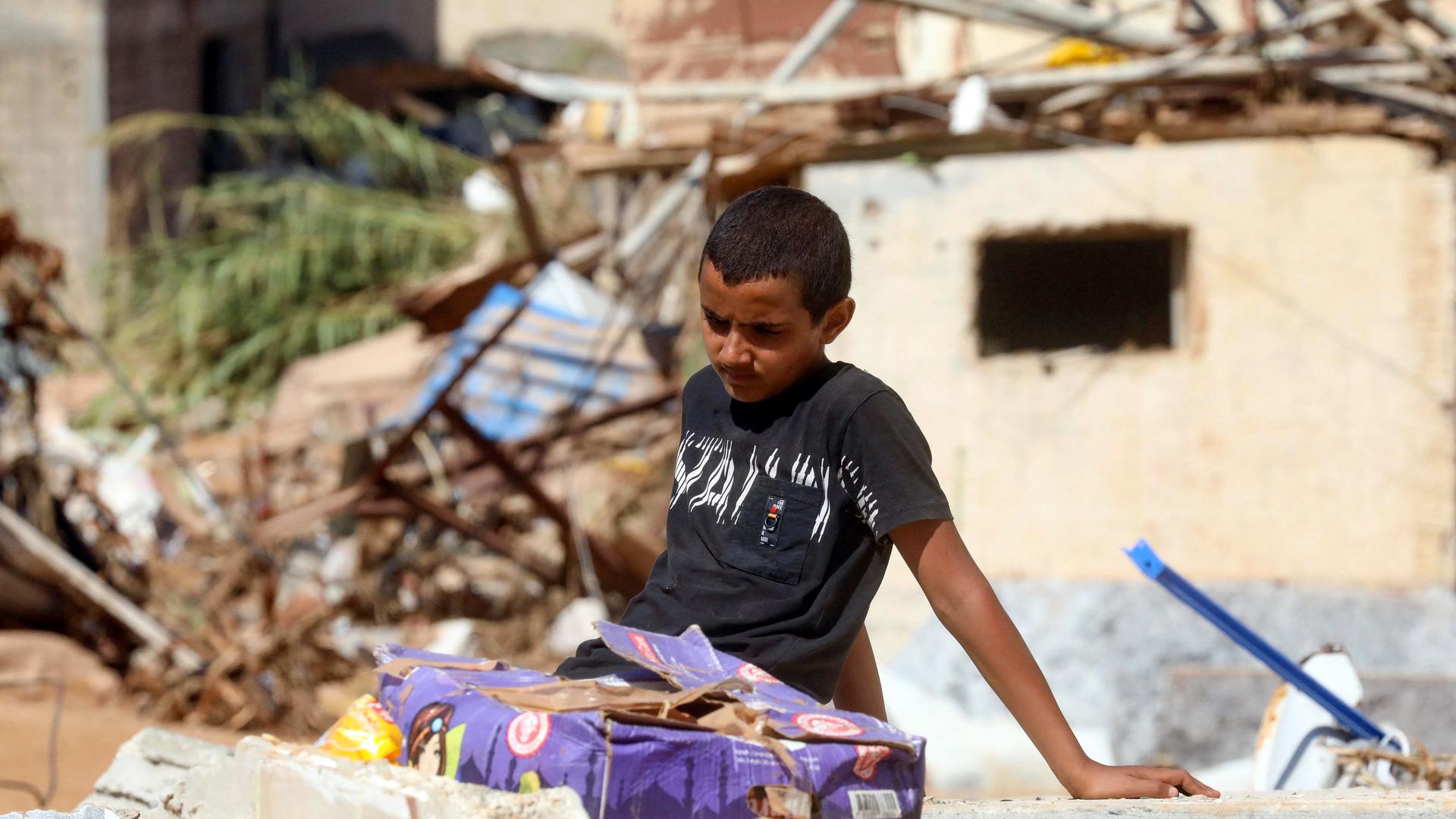 Ein Junge sitzt auf den Resten eines zerstörten Gebäudes. Im Hintergrund sind weitere von der Flut zerstörte Gebäude sowie Trümmerteile zu sehen.