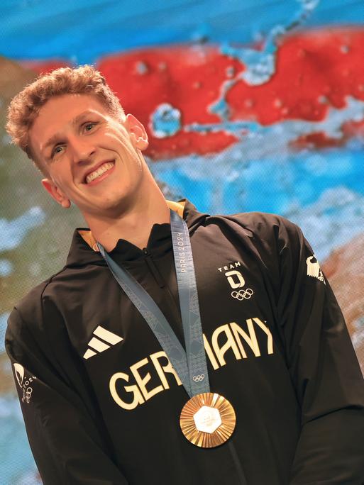 Der deutsche Goldmedaillengewinner Lukas Märtens freut sich über seine gewonne Medaille, die ihm um den Hals hängt. 