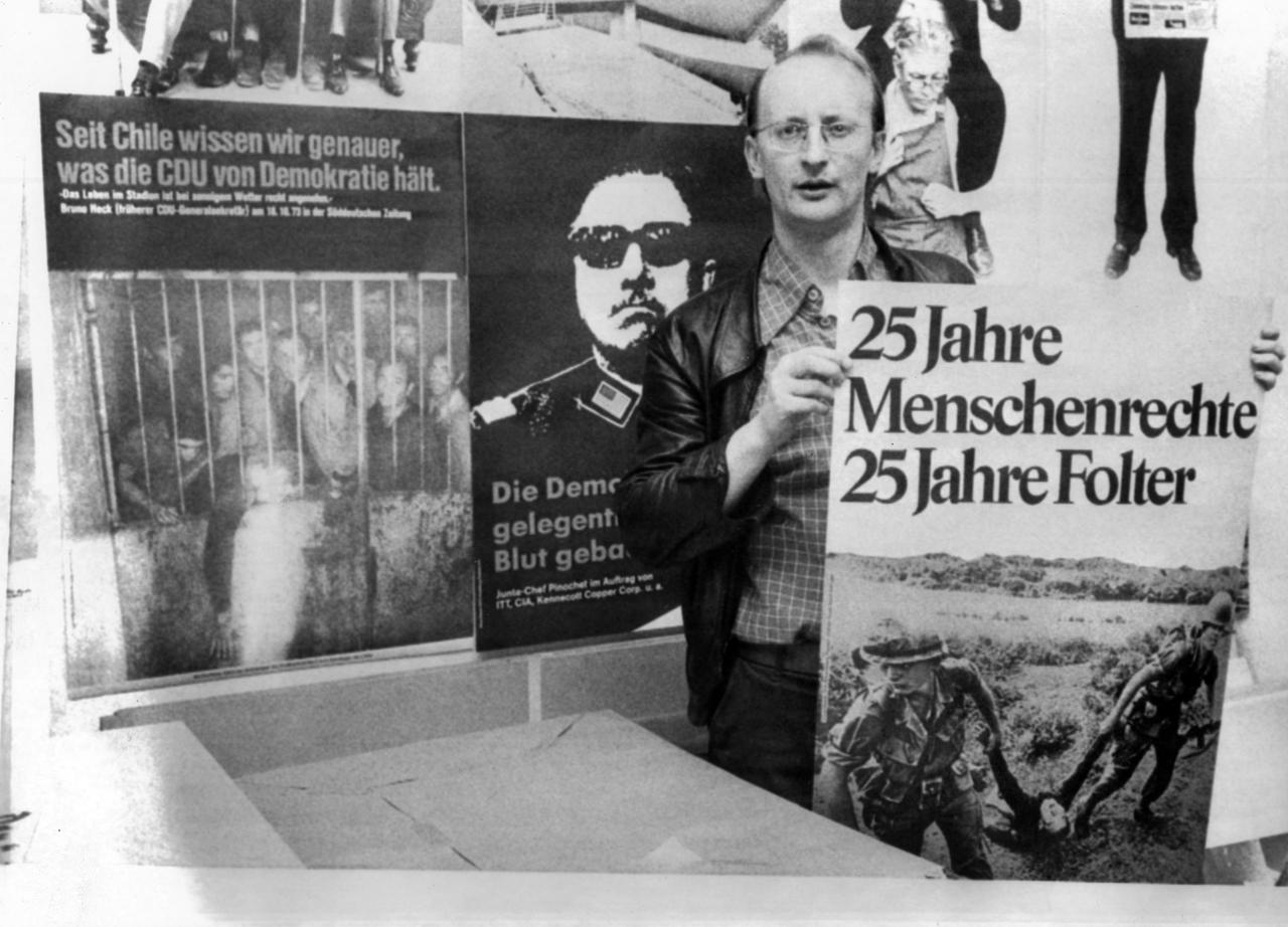 Der Heidelberger Karikaturist Klaus Staeck: Ein Mann hält ein Plakat in der Hand auf dem steht: 25 Jahre Menschenrechte, 25 Jahre Folter
