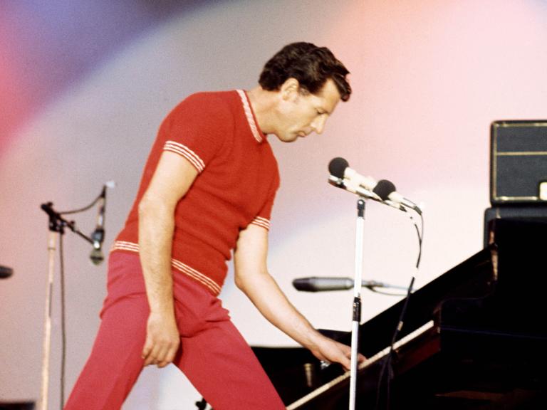 Jerry Lee Lewis spielt 1972 im Wembley Stadium in London. Er trägt einen roten Anzug und spielt im Stehen Piano.