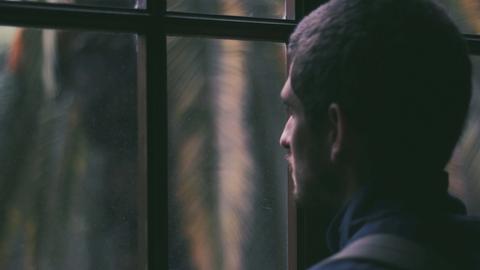 Ein Mann blickt bei Dunkelheit aus dem geschlossenen Fenster nach draußen.