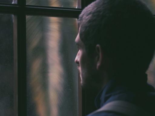 Ein Mann blickt bei Dunkelheit aus dem geschlossenen Fenster nach draußen.