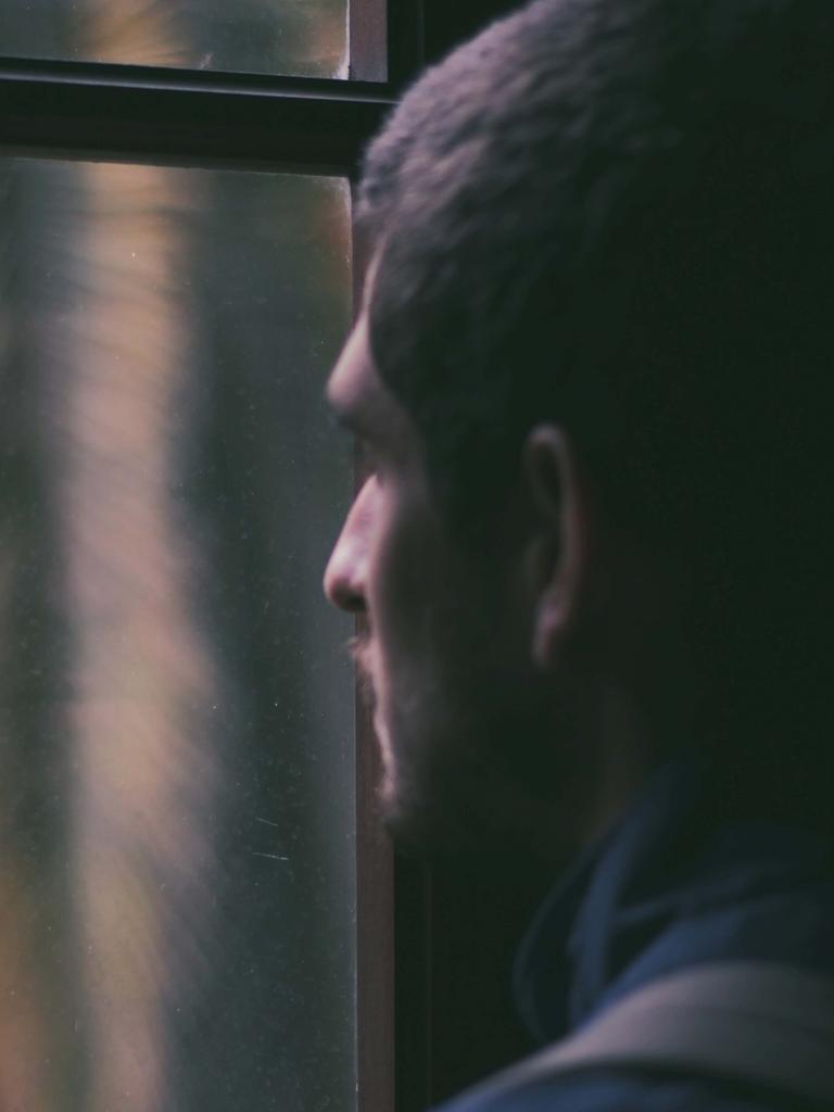 Ein Mann blickt bei Dunkelheit aus dem geschlossenen Fenster nach draußen.