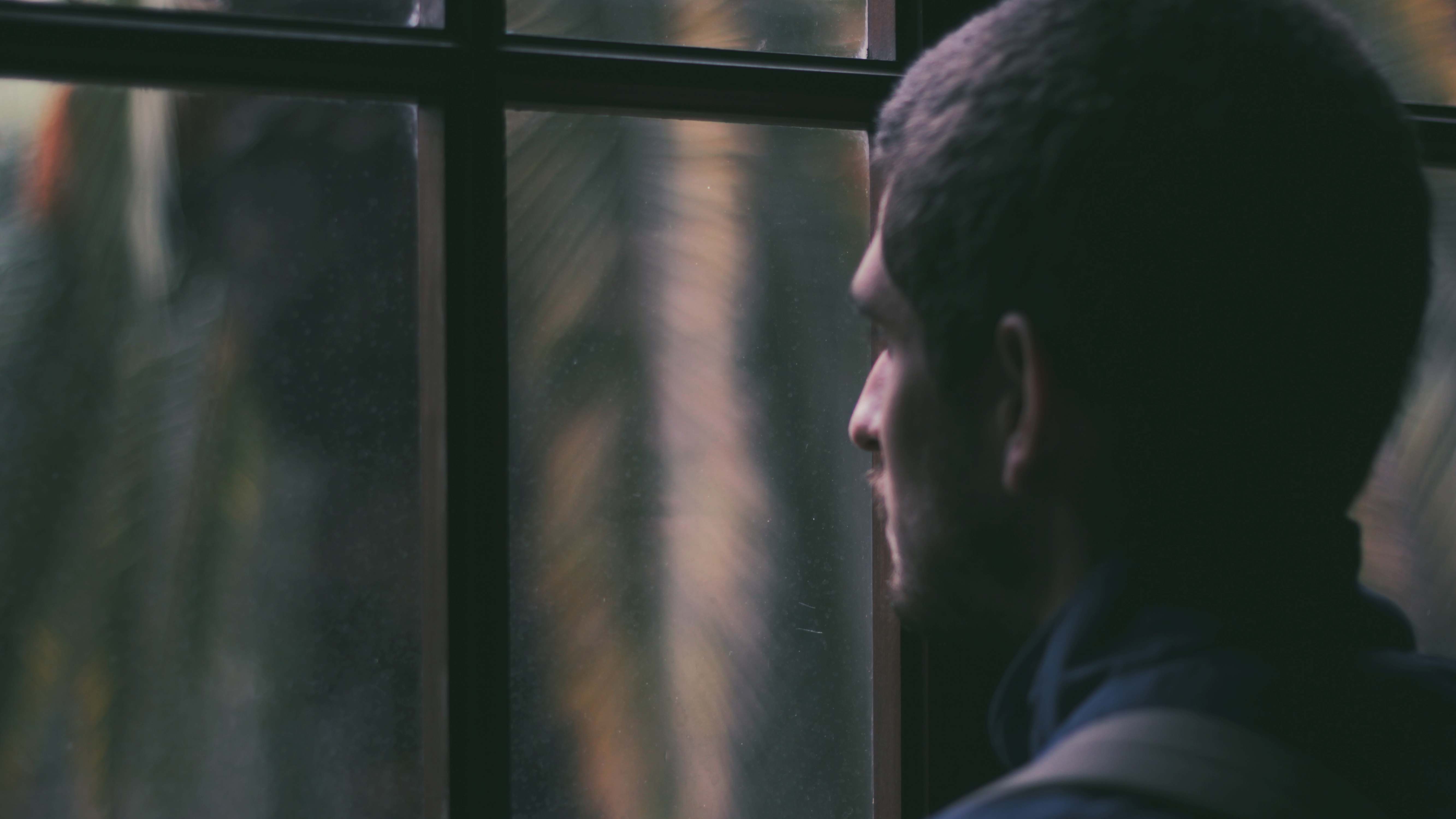 Ein Mann blickt bei Dunkelheit aus dem geschlossenen Fenster nach draußen.