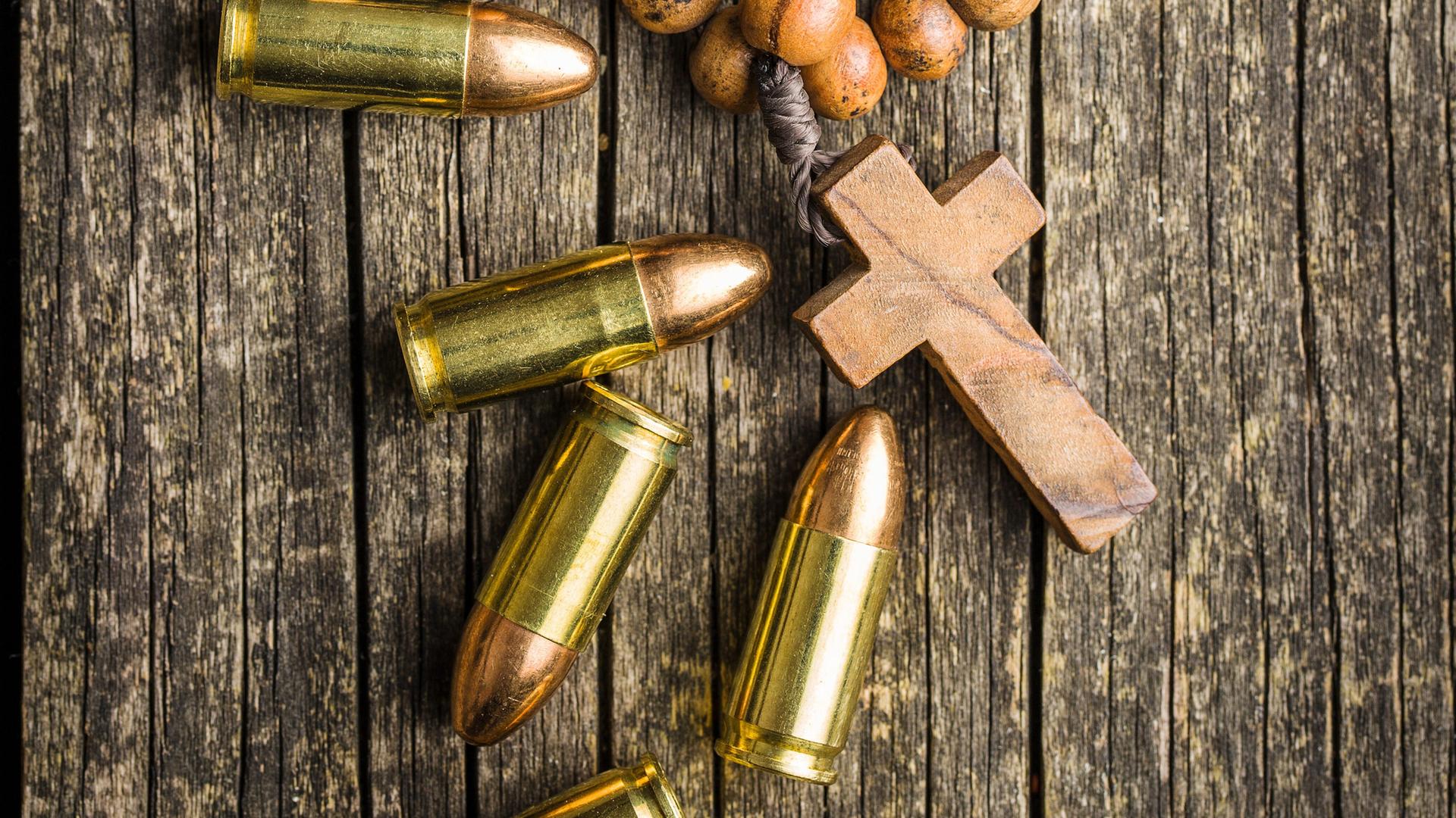Ein Rosenkranz und Patronenhülsen liegen auf einem Holzuntergrund