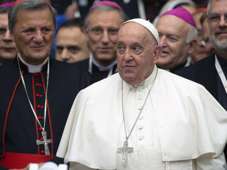 Papst Franziskus blickt zur Seite, neben ihm stehen andere Geistliche. (26.10.2024)