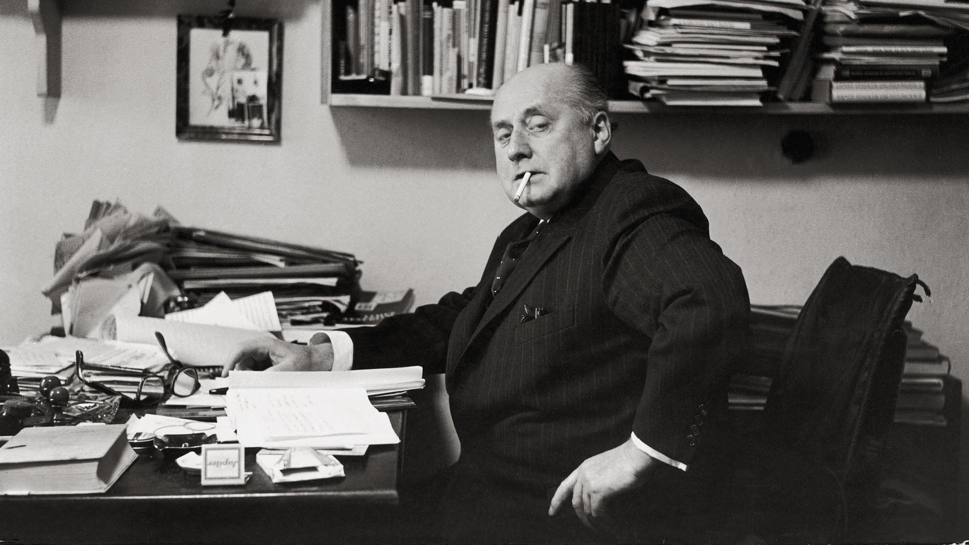 Gottfried Benn in seiner Berliner Wohnung. Regale und Tisch sind überfüllt mit Büchern und Notizen. Benn raucht. Gottfried Benn in seiner Berliner Wohnung. Regale und Tisch sind überfüllt mit Büchern und Notizen. Benn raucht.