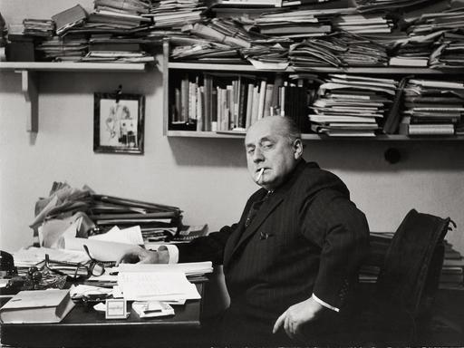 Gottfried Benn in seiner Berliner Wohnung. Regale und Tisch sind überfüllt mit Büchern und Notizen. Benn raucht. Gottfried Benn in seiner Berliner Wohnung. Regale und Tisch sind überfüllt mit Büchern und Notizen. Benn raucht.