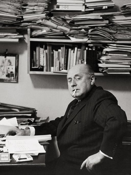Gottfried Benn in seiner Berliner Wohnung. Regale und Tisch sind überfüllt mit Büchern und Notizen. Benn raucht. Gottfried Benn in seiner Berliner Wohnung. Regale und Tisch sind überfüllt mit Büchern und Notizen. Benn raucht.
