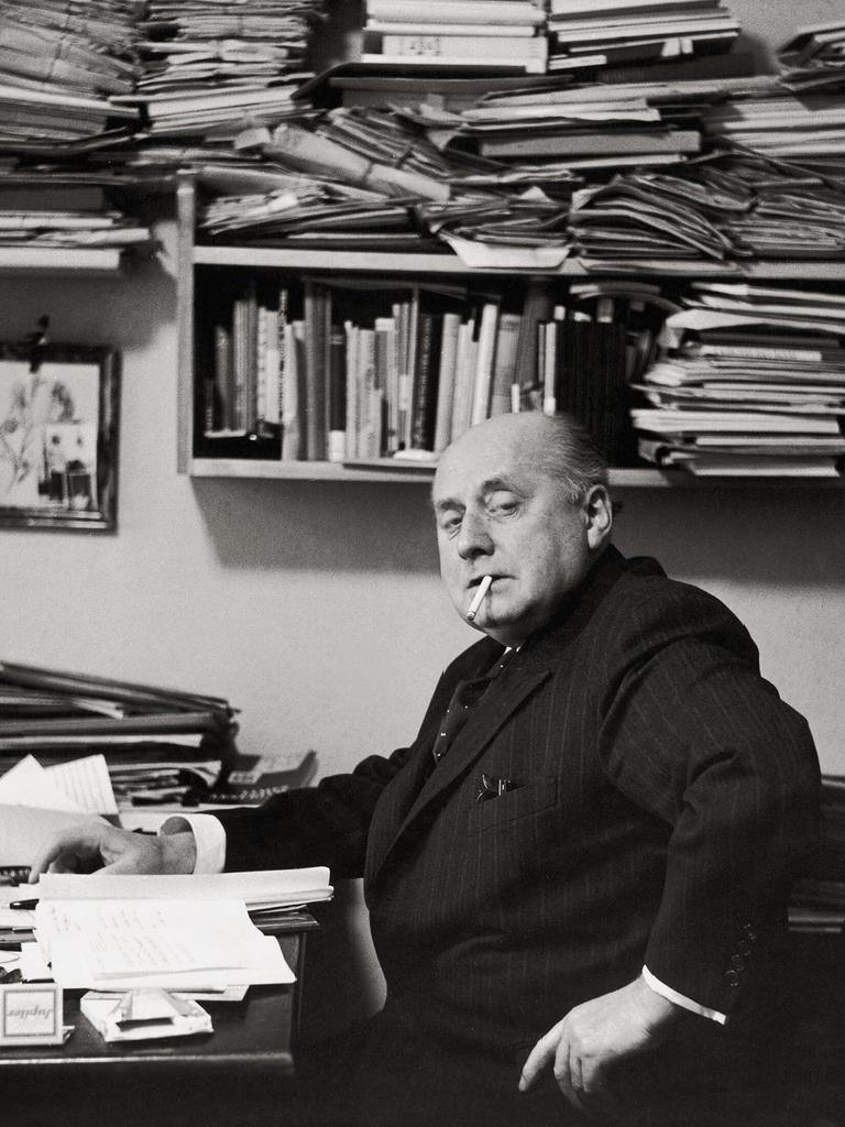 Gottfried Benn in seiner Berliner Wohnung. Regale und Tisch sind überfüllt mit Büchern und Notizen. Benn raucht. Gottfried Benn in seiner Berliner Wohnung. Regale und Tisch sind überfüllt mit Büchern und Notizen. Benn raucht.