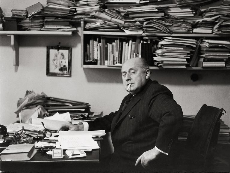 Gottfried Benn in seiner Berliner Wohnung. Regale und Tisch sind überfüllt mit Büchern und Notizen. Benn raucht. Gottfried Benn in seiner Berliner Wohnung. Regale und Tisch sind überfüllt mit Büchern und Notizen. Benn raucht.