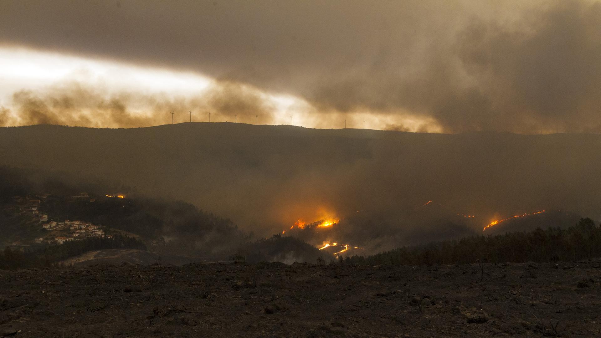 Feuer bei dem portugiesischen Dorf Pessegueiro, das teilweise von einem Waldbrand umgeben ist.