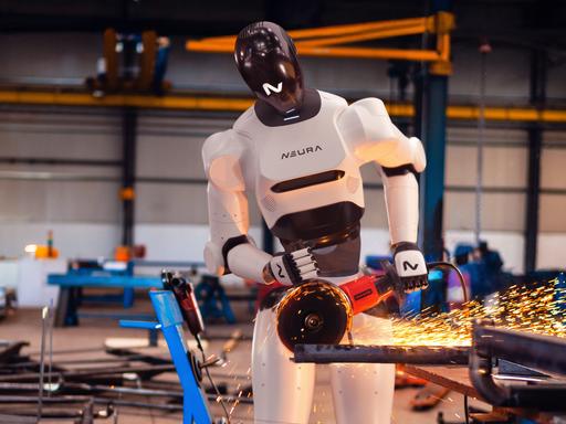 Ein humanoider Roboter (4NE1) der Firma "Neura Robotics" steht an einem Winkelschleifer in einer Industriehalle und verrichtet gefährliche Arbeiten, Funken fliegen direkt neben den Beinen des Roboters