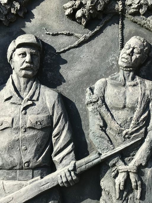 Ein Denkmal zur Erinnerung an den von deutschen Kolonialtruppen begangenen Völkermord an den Herero und Nama zeigt Gehängte neben einem schnauzbärtigen Soldaten.