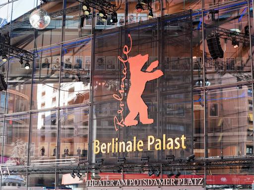 Auf einem Gebäude mit Glasfassade steht auf einem Plakat die Aufschrift Berlinale, daneben ein roter Bär. 