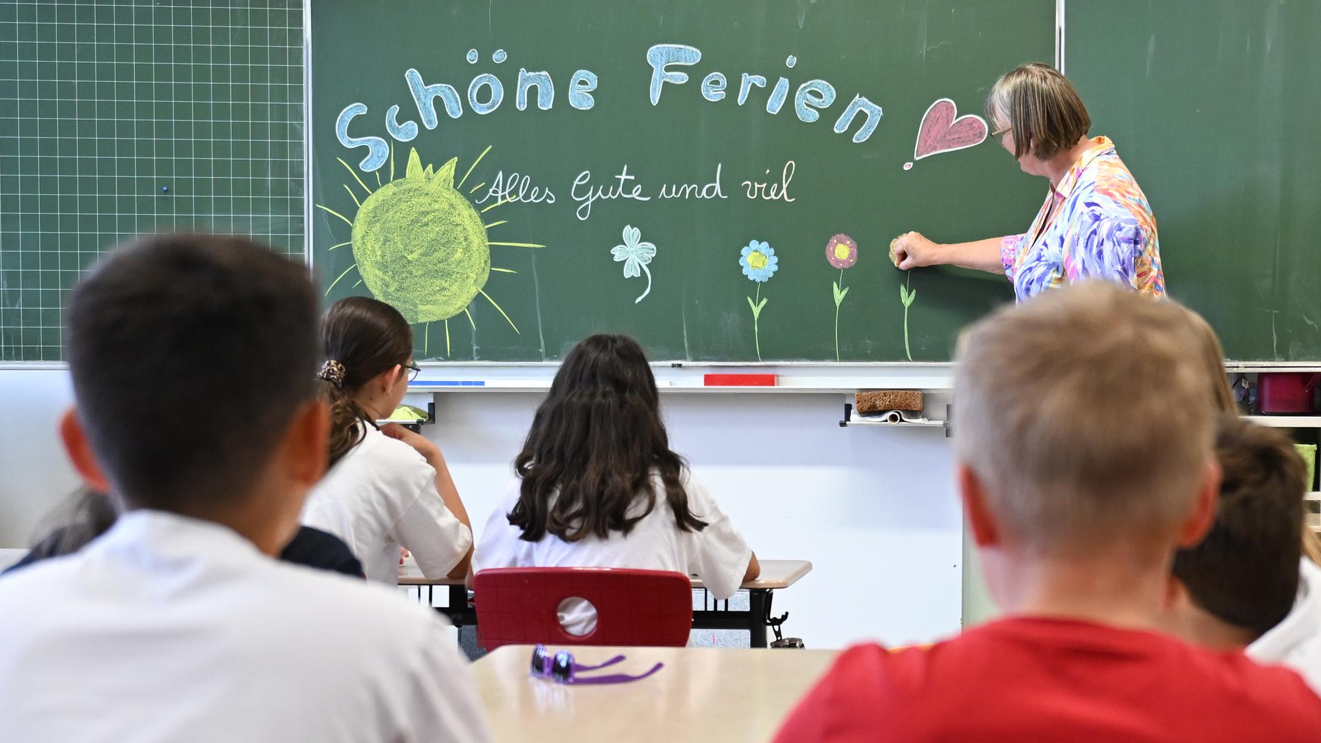 Schulkinder sitzen im Klassenzimmer am letzten Schultag vor den Sommerferien, eine Lehrerin schreibt an eine Tafel "Schöne Ferien Alles Gute und viel Glück". Schulkinder sitzen im Klassenzimmer am letzten Schultag vor den Sommerferien, eine Lehrerin schreibt an eine Tafel "Schöne Ferien Alles Gute und viel Glück".