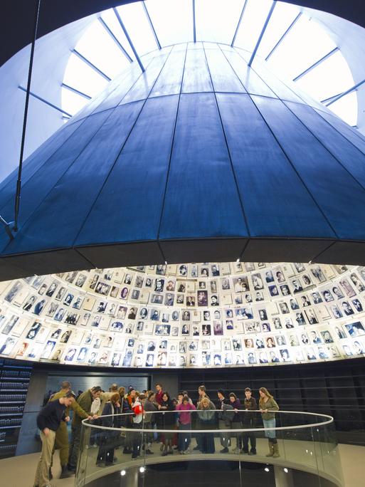 Blick auf eine Gruppe in Yad Vashem. Über ihnen schwebt ein Trichter mit Bildern von ermordeten Juden. Blick auf eine Gruppe in Yad Vashem. Über ihnen schwebt ein Trichter mit Bildern von ermordeten Juden.
