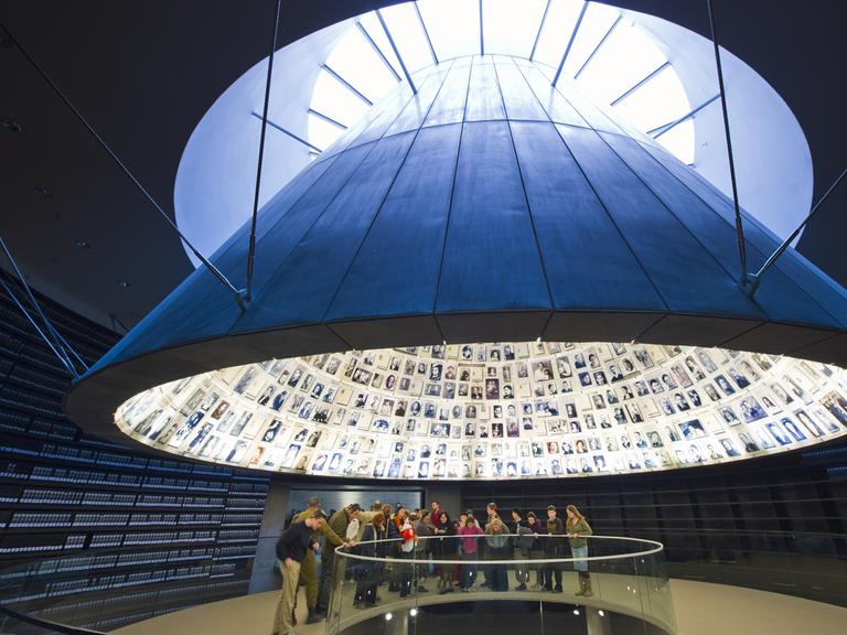 Blick auf eine Gruppe in Yad Vashem. Über ihnen schwebt ein Trichter mit Bildern von ermordeten Juden. Blick auf eine Gruppe in Yad Vashem. Über ihnen schwebt ein Trichter mit Bildern von ermordeten Juden.