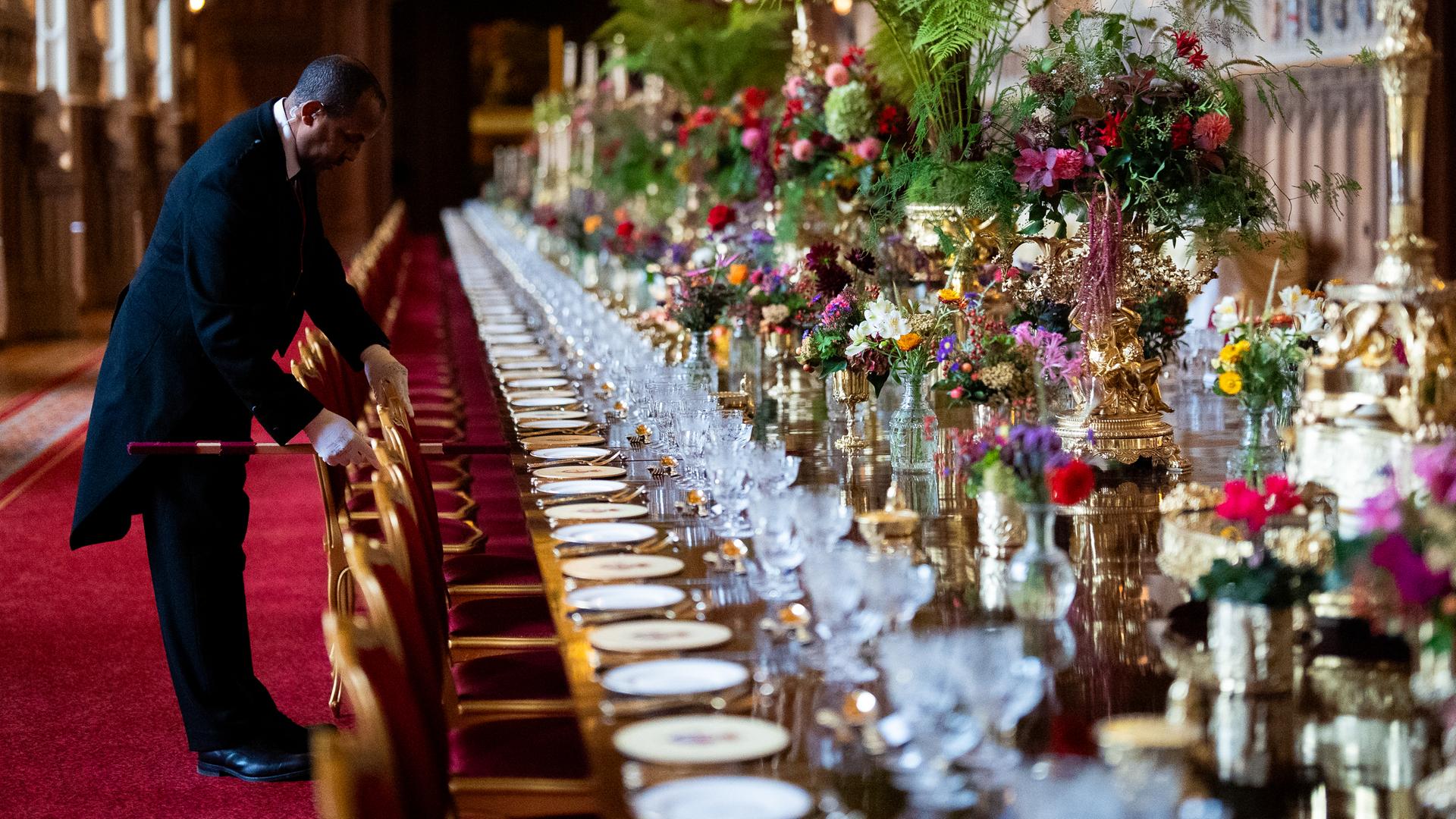 Die Stühle am elegant gedecktem Banketttisch in der St. Georges Hall werden von einem Angestellten im richtigen Abstand zueinander aufgestellt im Vorfeld eines Staatsbanketts im Windsor Castle in England. Die Stühle am elegant gedecktem Banketttisch in der St. Georges Hall werden von einem Angestellten im richtigen Abstand zueinander aufgestellt im Vorfeld eines Staatsbanketts im Windsor Castle in England.