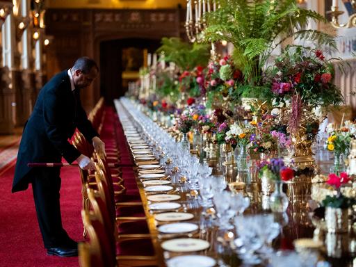 Die Stühle am elegant gedecktem Banketttisch in der St. Georges Hall werden von einem Angestellten im richtigen Abstand zueinander aufgestellt im Vorfeld eines Staatsbanketts im Windsor Castle in England. 
