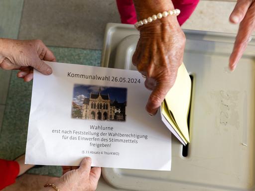 Eine Frau steckt ihre Wahlzettel in die Wahlurne.