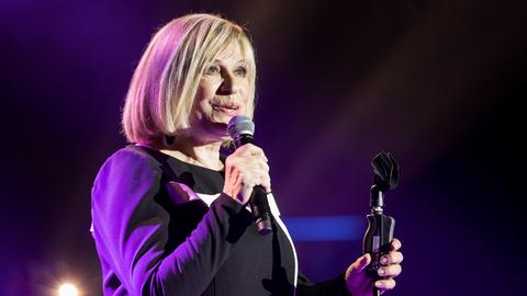 Mary Roos bei einem Konzert im Berliner Admiralspalast 2018. Sie hat ein Mikrofon in der Hand, der Hintergrund leuchtet blau.