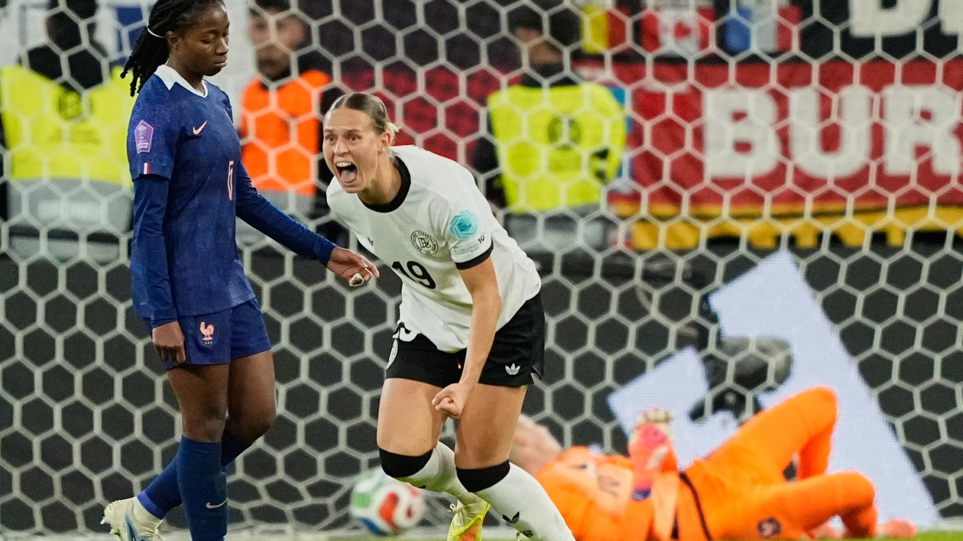 Die Fußballerin Klara Bühler jubelt nach einem Tor im Trikot des deutschen National-Teams. Im Hintergrund sind eine am Boden liegende Torhüterin und eine enttäuschte gegnerische Spielerin zu sehen.