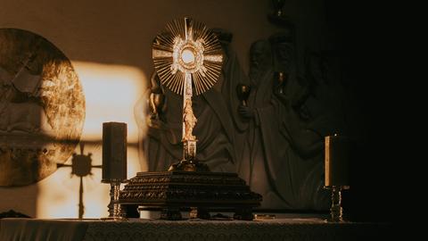 Licht durch ein Fenster fällt auf eine goldene Monstranz, die auf einem Altarsockel steht.