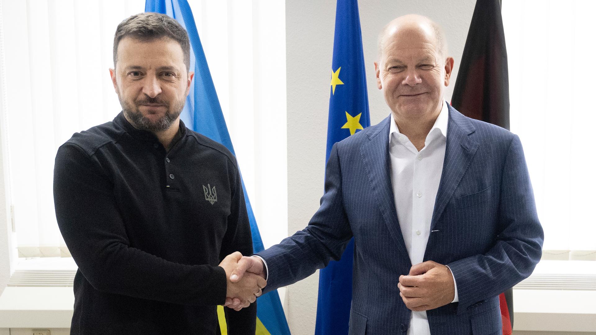 Bundeskanzler Olaf Scholz und der ukrainische Präsident Wolodymyr Selenskyj geben sich bei einem Treffen auf dem Frankfurter Flughafen die Hand und schauen in die Kameras. 